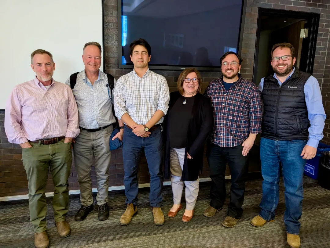 A doctoral student stands with their examination committee in a university meeting room following a successful PhD qualifying exam.