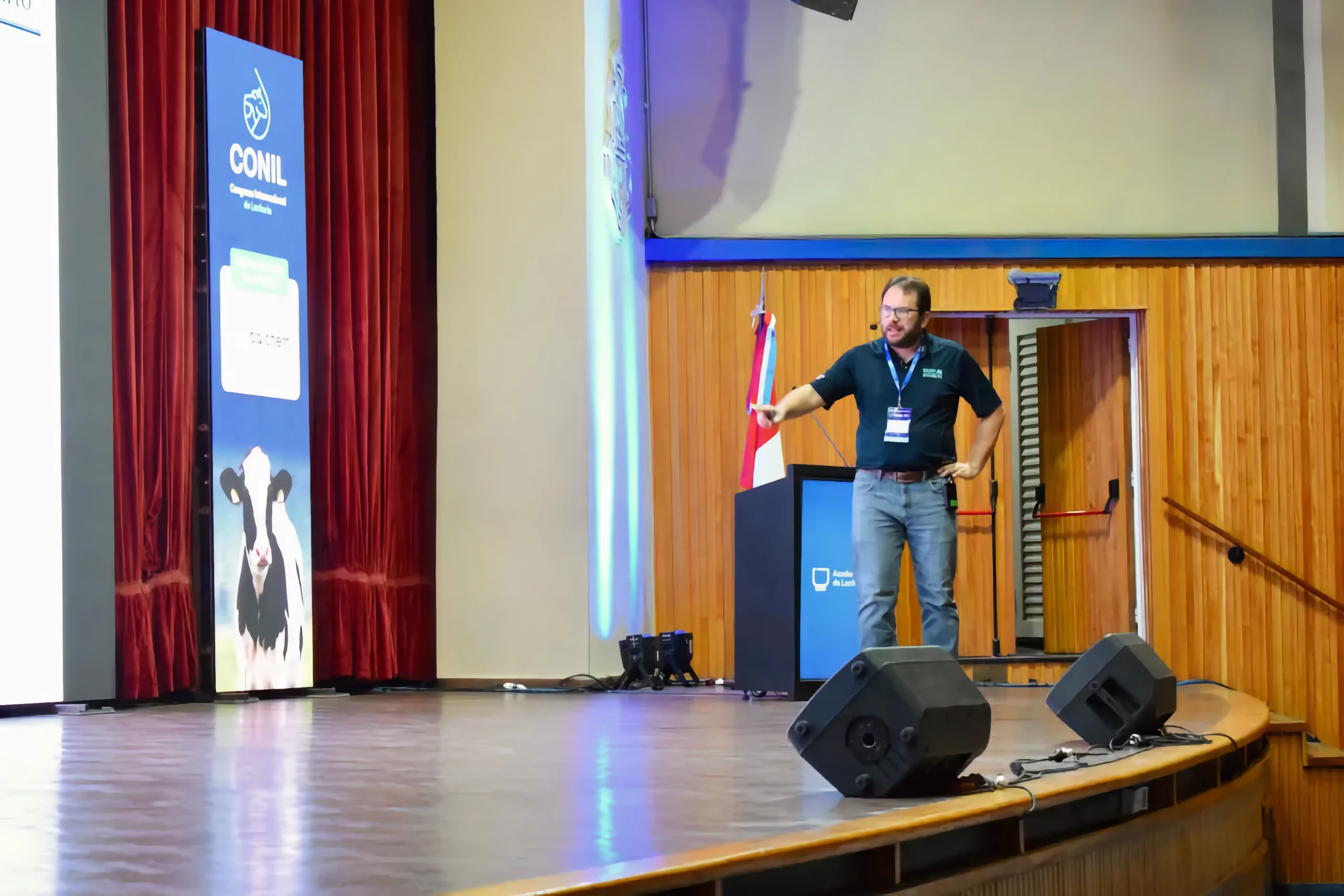 Dr. Ribeiro at CONIL 2025, delivering his presentation on a stage next to a digital banner featuring a Holstein cow.