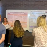 Outreach A female researcher presenting a scientific poster about dairy cow welfare and production to a group of colleagues during an academic seminar.