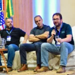 Outreach A panel of three researchers participating in a discussion at the Conil 2025 conference, with one expert speaking into a microphone while seated on a stage decorated with international flags.