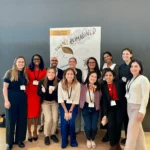 Outreach A diverse group of researchers and professionals posing together in front of a "Resilience Reimagined" poster at the Arrell Food Summit 2025.