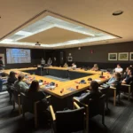 Outreach A group of university researchers and students participate in a lab meeting, viewing a presentation titled "Perspective tools for identification of problems" in a conference room with a large square conference table.
