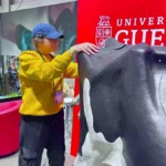 Outreach Kylie wearing a University of Guelph sweater and blue cap interacts with a life-sized Holstein cow model at an educational exhibit during the Royal Winter Fair 2025.