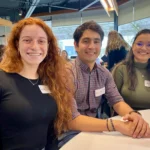 Outreach Three graduate students smile while seated at a table during the Animal Biosciences Research Graduate Student Symposium 2024.