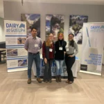 Outreach Four university researchers pose together in front of a "Dairy at Guelph" display and institutional banners during the Dairy at Guelph Research Showcase 2024.