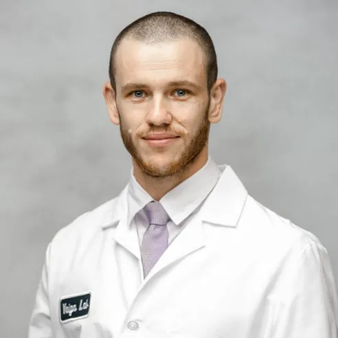 Members A professional headshot of a male researcher with a short beard, wearing a white laboratory coat over a dress shirt and tie, set against a neutral grey background.