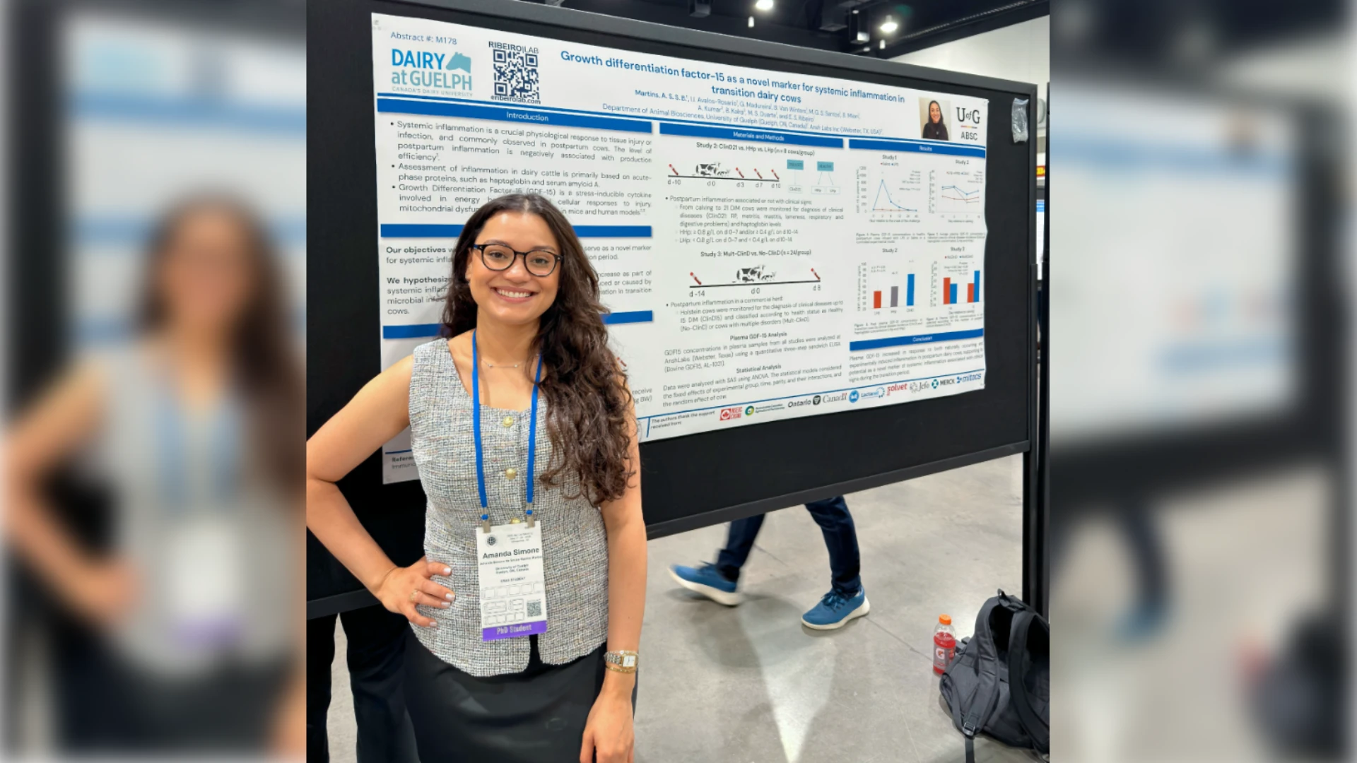Ribeiro Lab at ADSA 2026 Wrap-Up A smiling female PhD student with glasses standing with her hand on her hip next to her research poster at a conference. The poster features University of Guelph and Ribeiro Lab branding, titled 'Growth differentiation factor-15 as a novel marker for systemic inflammation in transition dairy cows'.