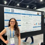 Outreach A smiling female PhD student with glasses standing with her hand on her hip next to her research poster at a conference. The poster features University of Guelph and Ribeiro Lab branding, titled 'Growth differentiation factor-15 as a novel marker for systemic inflammation in transition dairy cows'.