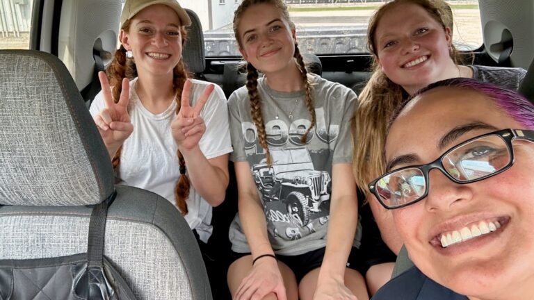 Selfie of four female researchers sitting inside a vehicle, smiling and gesturing peace signs on their way to a field visit.
