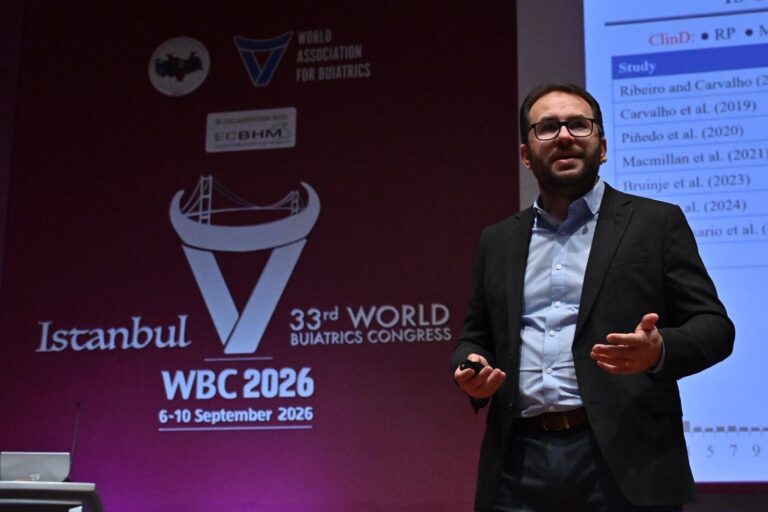 Medium close-up of Dr. Ribeiro with glasses and a dark blazer speaking with expressive hand gestures in front of the 33rd World Buiatrics Congress (WBC 2026) backdrop in Istanbul.